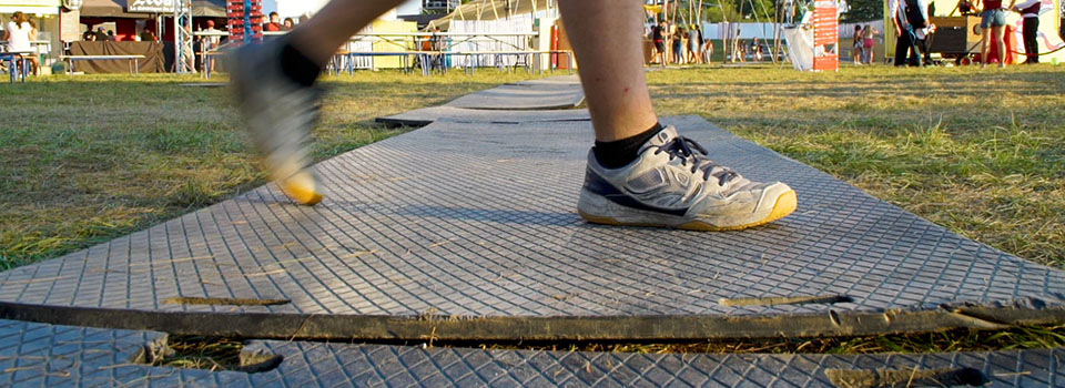 Plaque de roulage inadaptée pour l’accessibilité Une personne marche sur un cheminement avec des plaques de roulage placées sur un terrain herbeux. Les plaques sont disjointes, non planes entrainant un risque de chute et un accès chaotique pour les personnes en fauteuil